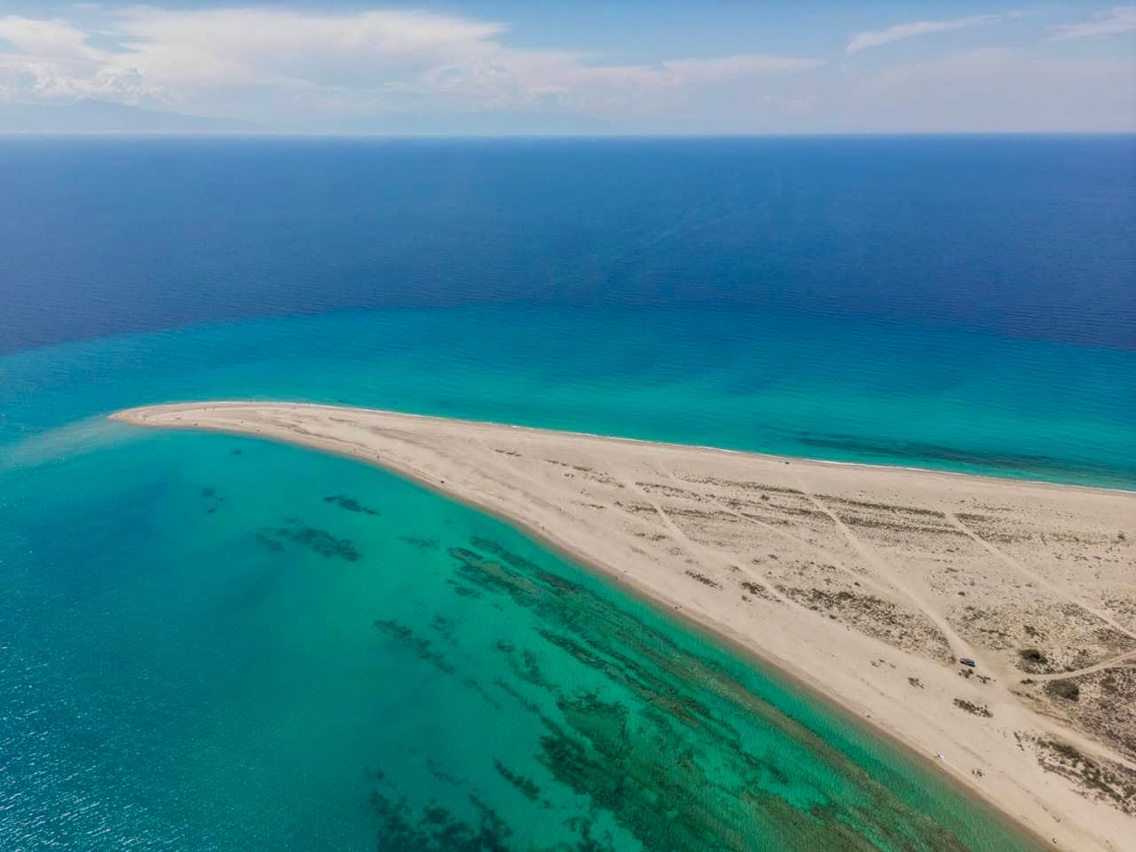 Kassandra Halkidiki: aerial of a long white sand spit curving into the sea, turquoise shallows with seagrass on one side and deep blue water on the other