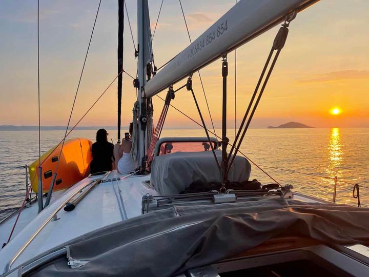 Two guests on the foredeck of a sailing yacht watching the sun set over the sea, sunset sailing cruise Halkidiki